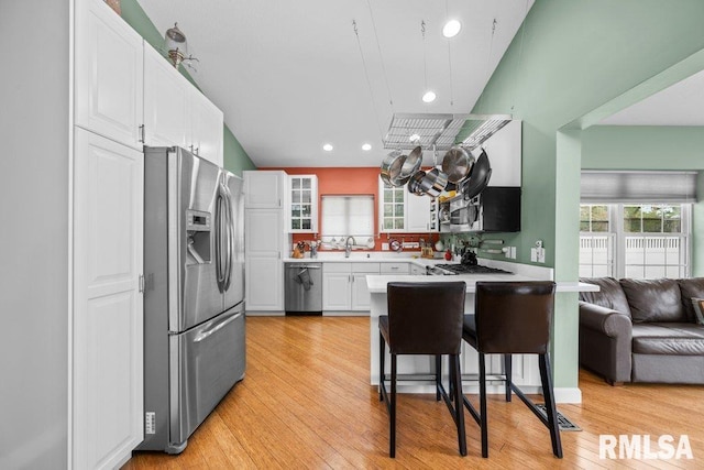 kitchen with appliances with stainless steel finishes, light hardwood / wood-style flooring, a kitchen bar, and white cabinets