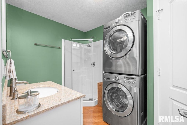 washroom with stacked washer / drying machine, a textured ceiling, sink, and light hardwood / wood-style floors