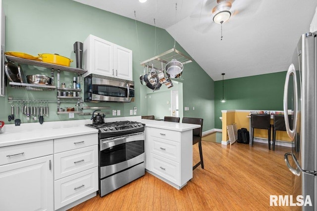 kitchen with light hardwood / wood-style flooring, kitchen peninsula, vaulted ceiling, white cabinets, and appliances with stainless steel finishes