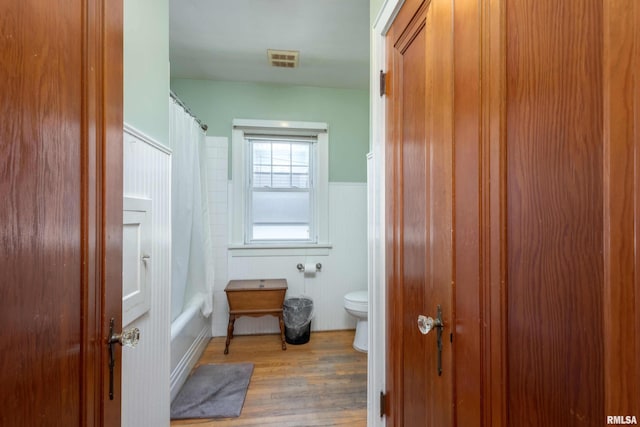 bathroom featuring toilet, shower / bathtub combination with curtain, and hardwood / wood-style floors