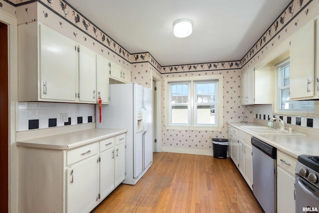 kitchen featuring stainless steel appliances, backsplash, sink, white cabinetry, and light hardwood / wood-style floors