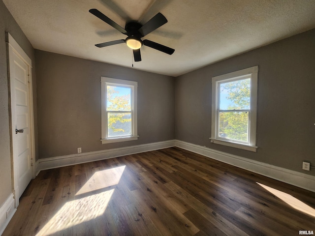 empty room featuring a textured ceiling, dark wood-type flooring, and a wealth of natural light