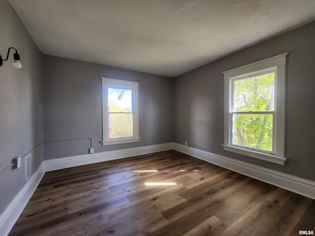 unfurnished room featuring a textured ceiling, a healthy amount of sunlight, and dark hardwood / wood-style flooring