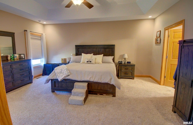 bedroom with light carpet, a tray ceiling, and ceiling fan