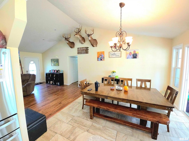 dining space with an inviting chandelier, light wood-type flooring, and vaulted ceiling