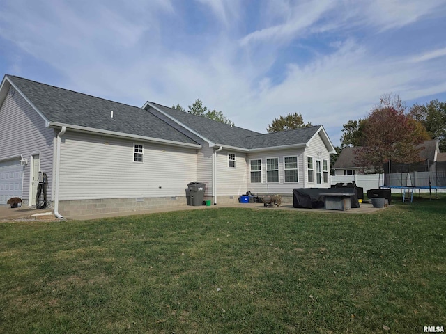 back of house featuring a hot tub, a trampoline, a lawn, and a garage