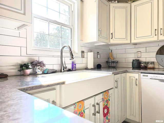 kitchen with white dishwasher, sink, cream cabinetry, and backsplash