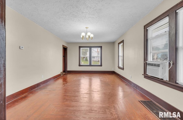 unfurnished room with hardwood / wood-style flooring, cooling unit, a textured ceiling, and a notable chandelier