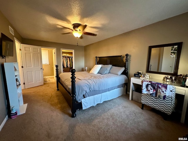 carpeted bedroom with a closet, ceiling fan, a textured ceiling, and a walk in closet