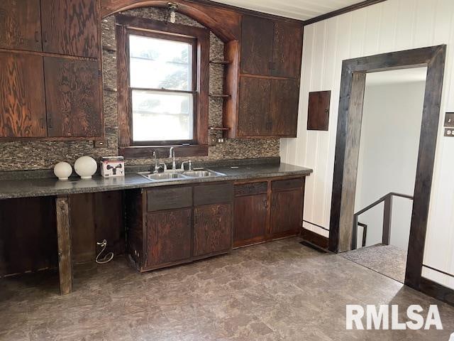 kitchen with decorative backsplash, ornamental molding, sink, dark brown cabinetry, and wood walls