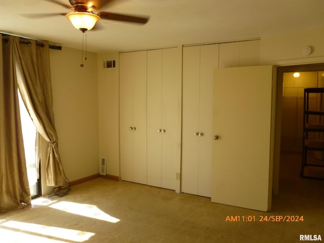 unfurnished bedroom with multiple closets, light colored carpet, and ceiling fan