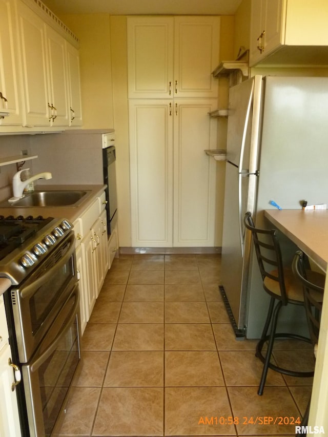 kitchen with sink, white cabinets, stainless steel appliances, and light tile patterned floors