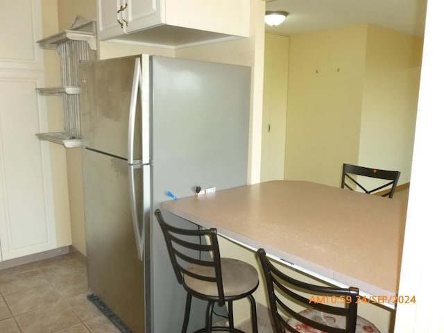 kitchen featuring a breakfast bar, stainless steel refrigerator, light tile patterned floors, and white cabinets