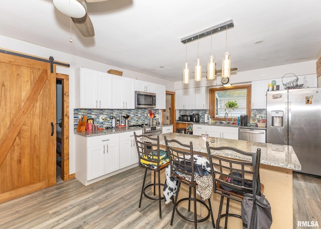 kitchen featuring a center island, a barn door, light hardwood / wood-style flooring, white cabinets, and appliances with stainless steel finishes