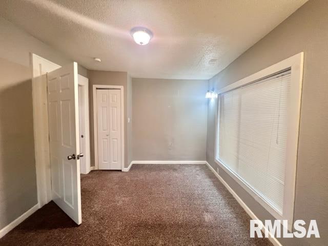 unfurnished bedroom with dark colored carpet, a textured ceiling, and a closet