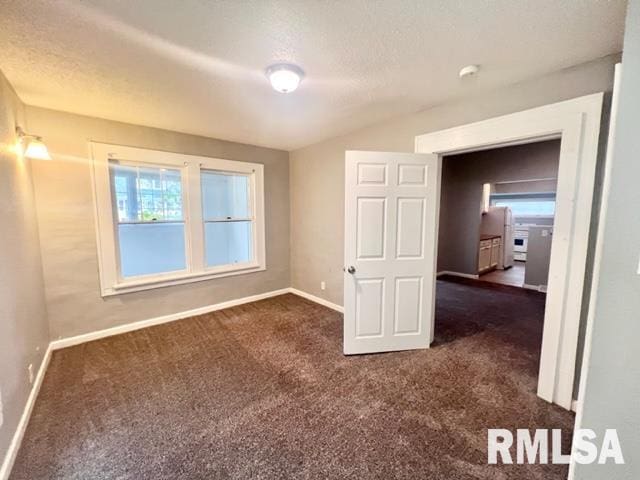 spare room with a textured ceiling and dark colored carpet