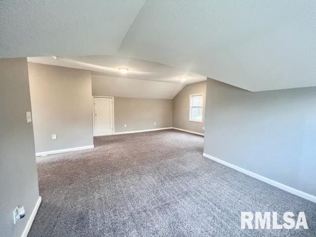 additional living space featuring a textured ceiling, vaulted ceiling, and dark carpet