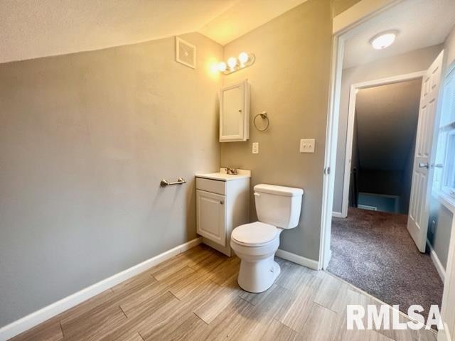 bathroom with toilet, vanity, vaulted ceiling, and wood-type flooring