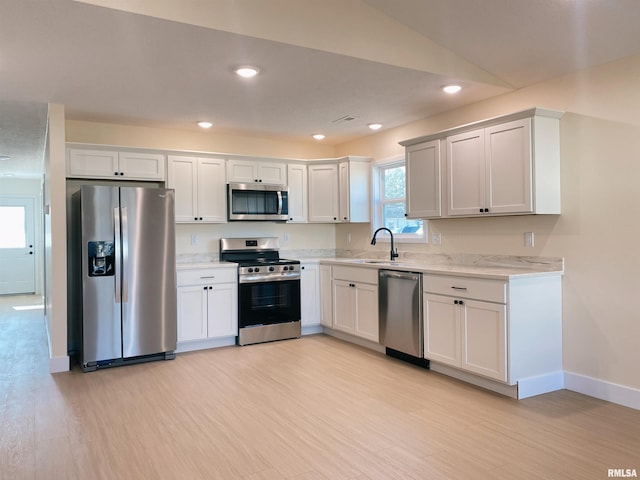 kitchen featuring sink, stainless steel appliances, light hardwood / wood-style flooring, vaulted ceiling, and white cabinets