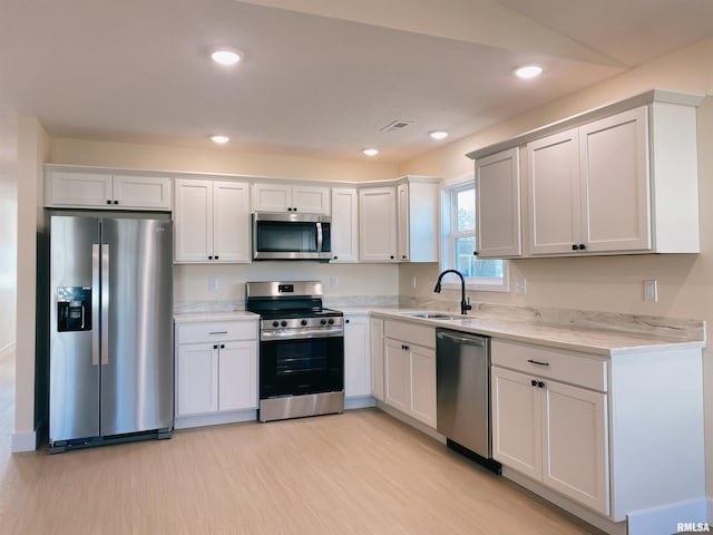 kitchen featuring white cabinets, sink, vaulted ceiling, light stone countertops, and stainless steel appliances