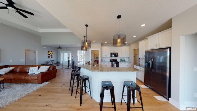 kitchen with hanging light fixtures, stainless steel appliances, an island with sink, sink, and white cabinetry