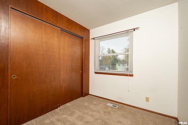 unfurnished bedroom with wood walls, carpet flooring, a closet, and a textured ceiling