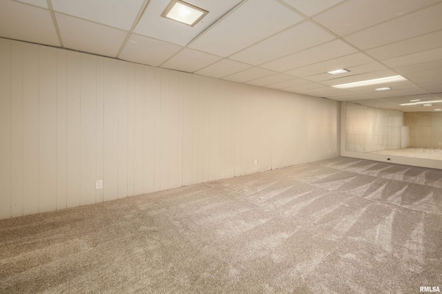 basement featuring carpet flooring, wooden walls, and a drop ceiling