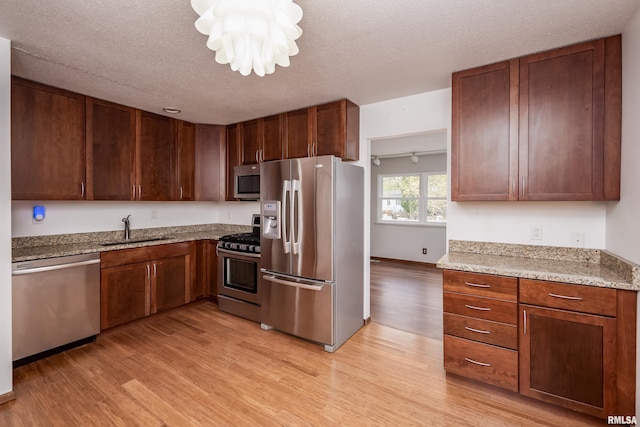 kitchen featuring stainless steel appliances, light hardwood / wood-style floors, sink, light stone countertops, and a textured ceiling