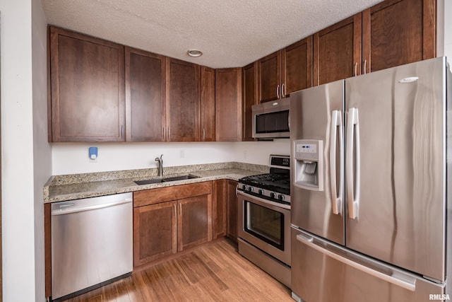 kitchen with light stone counters, stainless steel appliances, a textured ceiling, sink, and light hardwood / wood-style floors