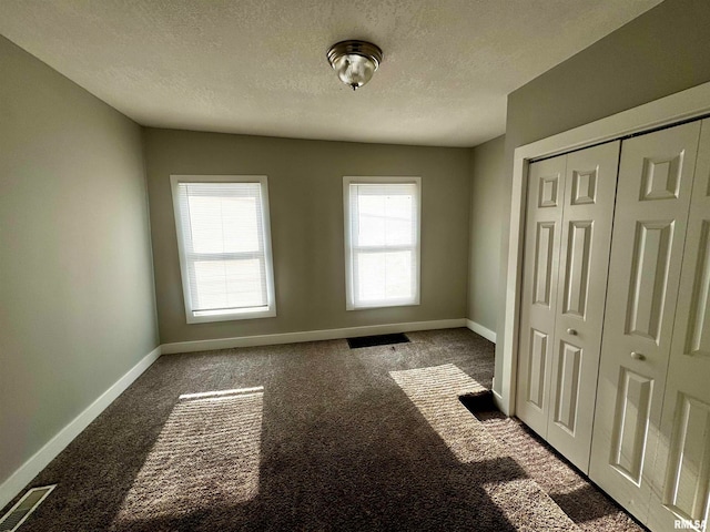 unfurnished bedroom with a textured ceiling, a closet, and dark carpet