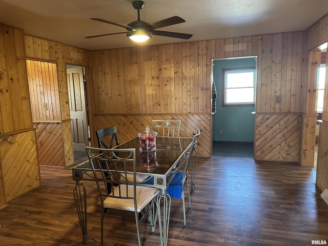 dining room featuring ceiling fan, wood walls, and dark wood-type flooring