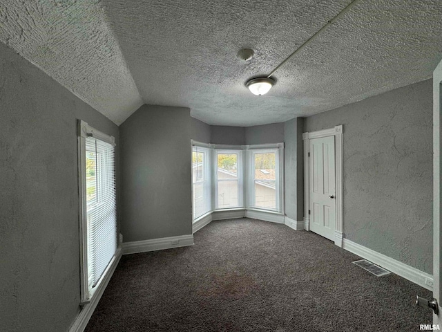 spare room featuring dark colored carpet, a textured ceiling, and vaulted ceiling