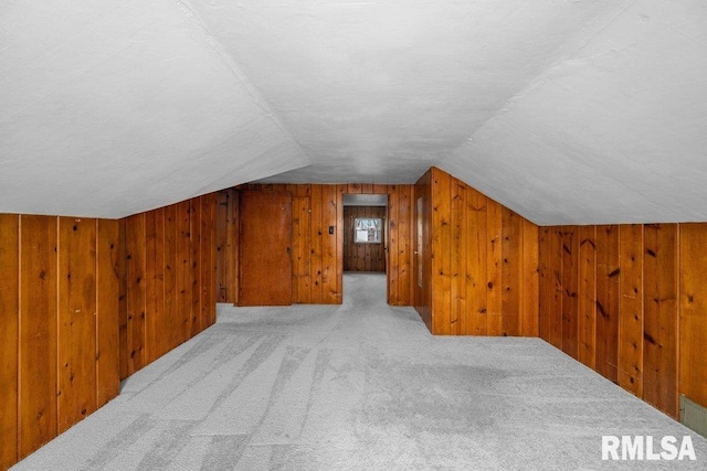 additional living space with light carpet, lofted ceiling, and wood walls