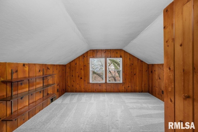 additional living space with wood walls, light colored carpet, and lofted ceiling