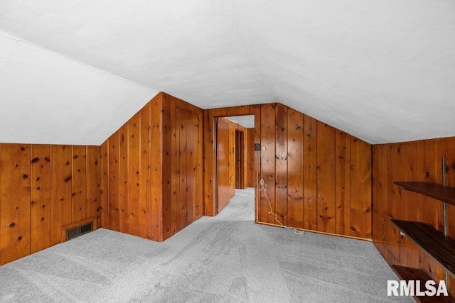 bonus room featuring light colored carpet, vaulted ceiling, and wood walls