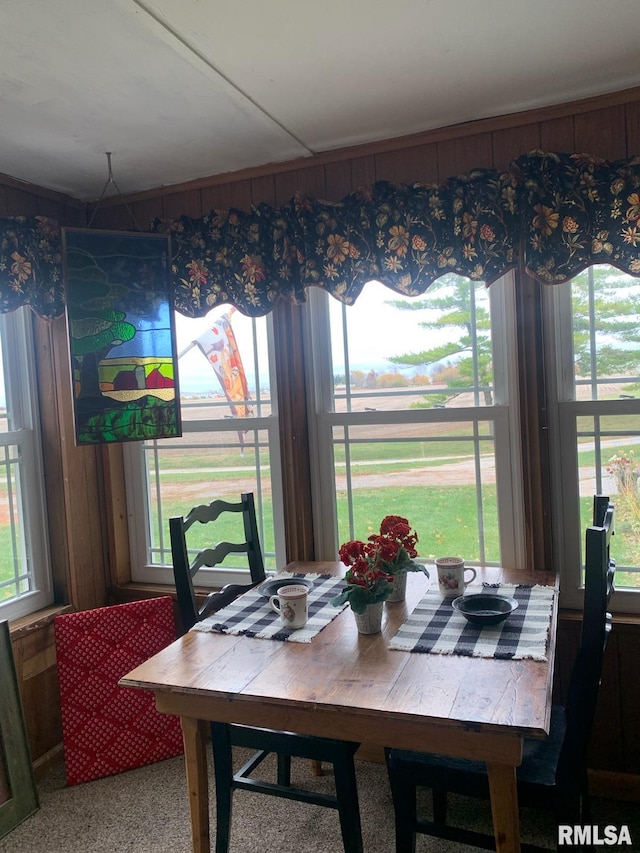 carpeted dining area featuring wood walls