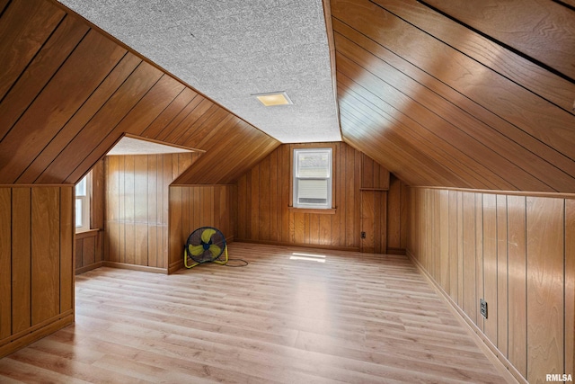 bonus room featuring light hardwood / wood-style flooring, wood walls, a textured ceiling, and lofted ceiling