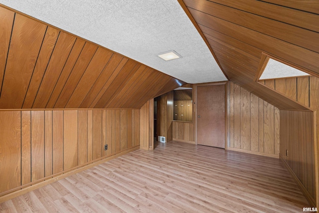 bonus room with wood walls, a textured ceiling, and light hardwood / wood-style flooring