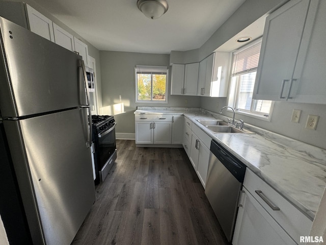 kitchen with light stone counters, appliances with stainless steel finishes, dark hardwood / wood-style flooring, sink, and white cabinets