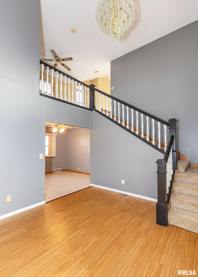 stairs featuring a high ceiling, hardwood / wood-style floors, and ceiling fan with notable chandelier