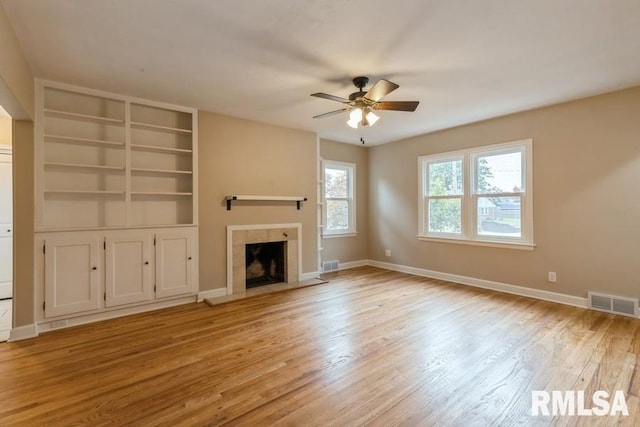 unfurnished living room featuring light hardwood / wood-style floors, ceiling fan, a tile fireplace, and built in features