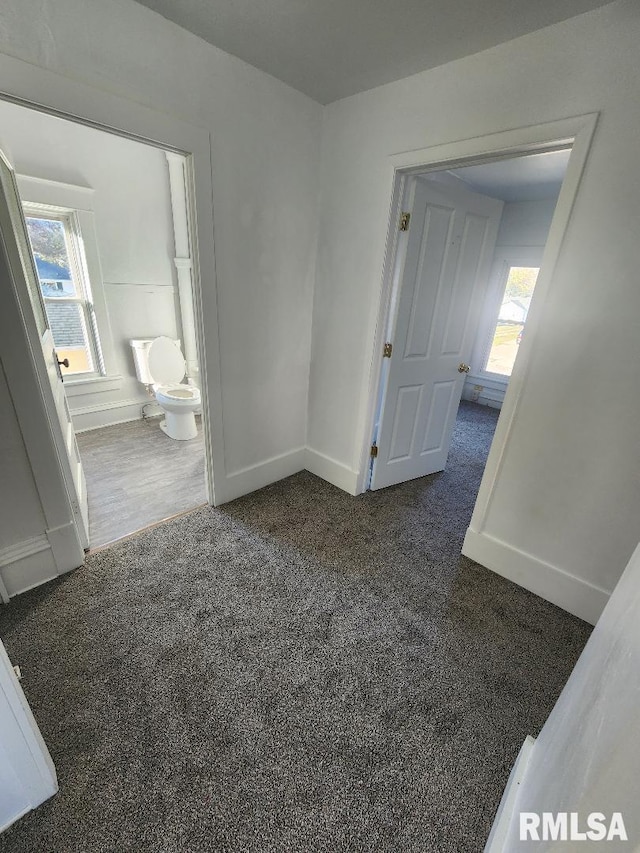 interior space with multiple windows, connected bathroom, and dark carpet