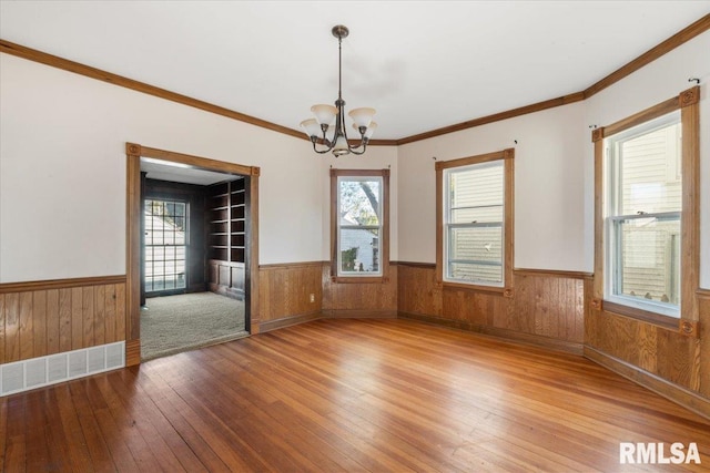 empty room featuring crown molding, wood-type flooring, a healthy amount of sunlight, and a chandelier