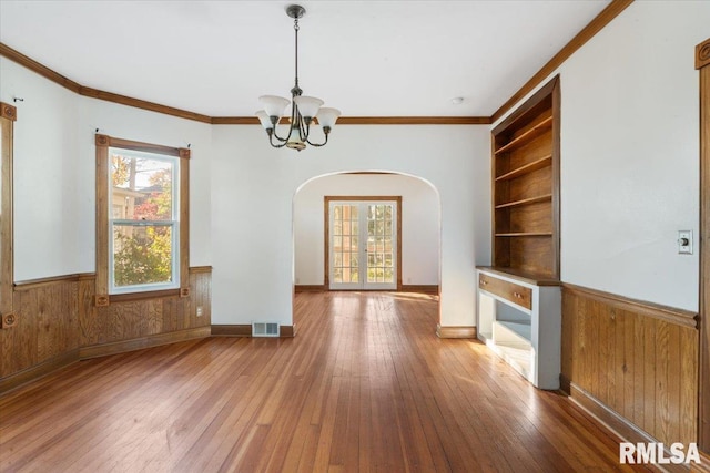 interior space featuring built in features, ornamental molding, wooden walls, an inviting chandelier, and hardwood / wood-style flooring