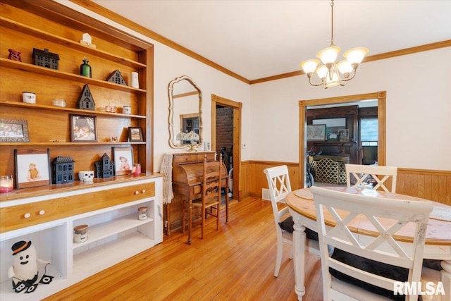 dining room with ornamental molding, light hardwood / wood-style floors, wooden walls, and an inviting chandelier