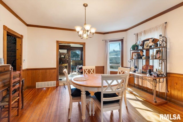 dining space with hardwood / wood-style flooring, a chandelier, wooden walls, and ornamental molding