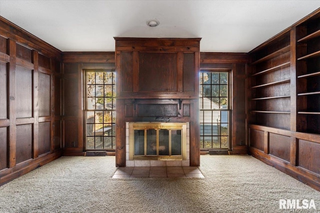 unfurnished living room featuring wood walls, a wealth of natural light, and carpet floors