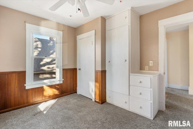 unfurnished bedroom with wood walls, ceiling fan, and light carpet