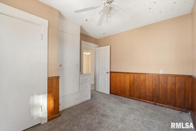 unfurnished bedroom featuring wood walls, ceiling fan, and light carpet