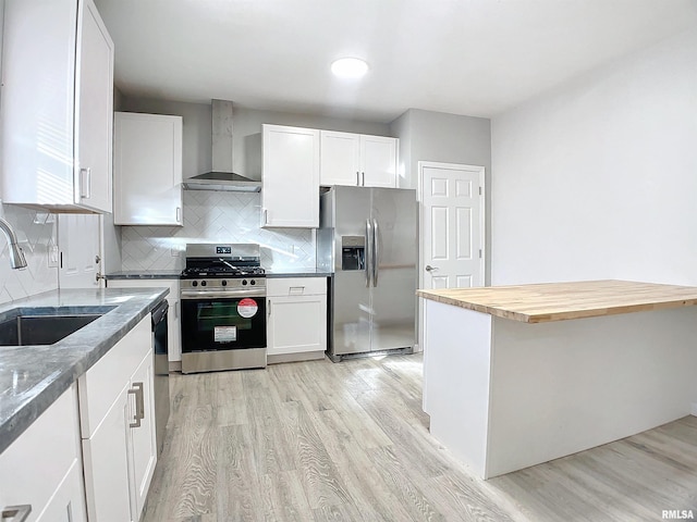 kitchen with butcher block counters, sink, white cabinetry, wall chimney exhaust hood, and appliances with stainless steel finishes